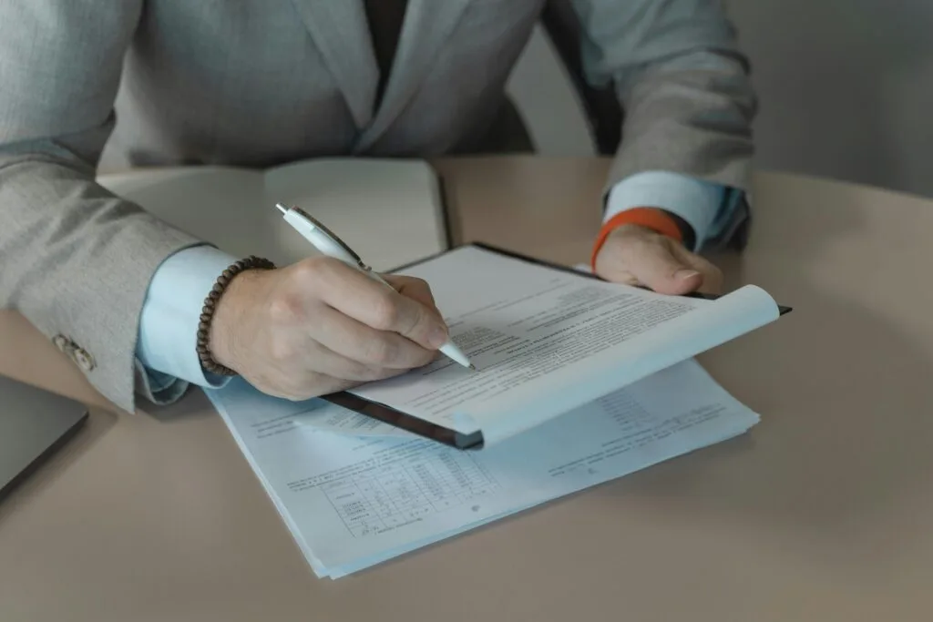 Close-up of business person signing documents at a desk with a pen.